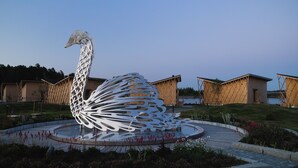 A large white sculpture of a swan in a circular water feature with a paved walkway and buildings in the background. - Bella Lake Resort (Kuopio)