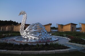 Una gran escultura blanca de un cisne en una fuente circular con un camino empedrado y edificios al fondo.