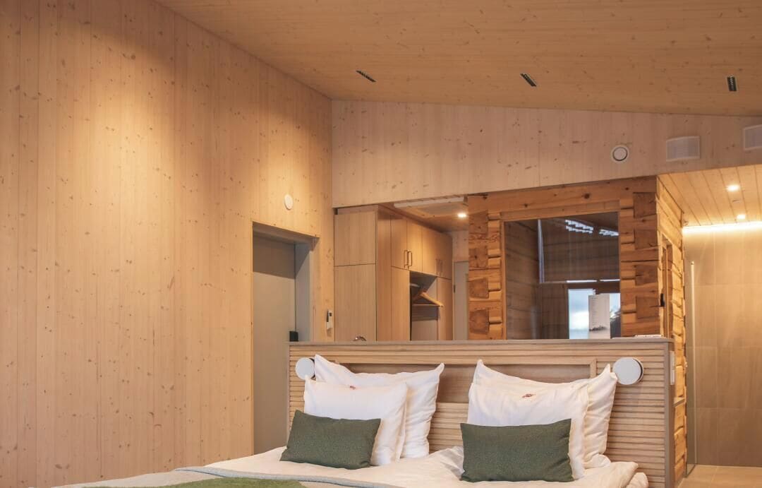 Une pièce aux murs lambrissés, avec un lit, un miroir et une vue sur une autre pièce.