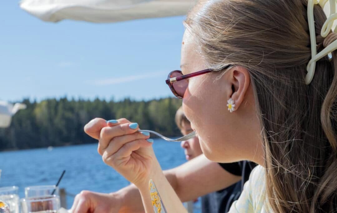 A person dining outdoors with a view of a body of water and trees in the background.