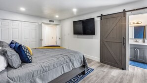 A bedroom with a bed, a TV, a wardrobe, and a bathroom visible through an open door. - Charming 3-bedroom house with AC, WiFi in fabulous Glendale (Glendale)