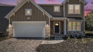 Une maison à deux étages avec une façade en pierre, un garage et une véranda à l’avant.