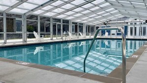 Une piscine intérieure dotée d’un plafond en verre transparent, d’un escalier d’accès et de chaises longues.