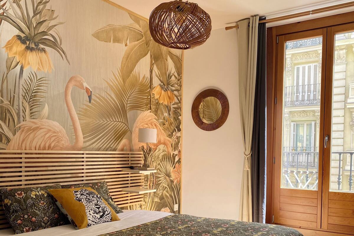 A bedroom with a bed, a hanging light fixture, a wall mural, a window, and a door.