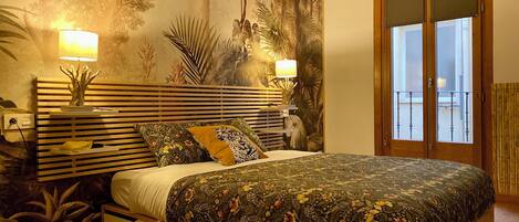 A bedroom with a bed, two bedside lamps, a nightstand, a wall mural, and a sliding door to a balcony.