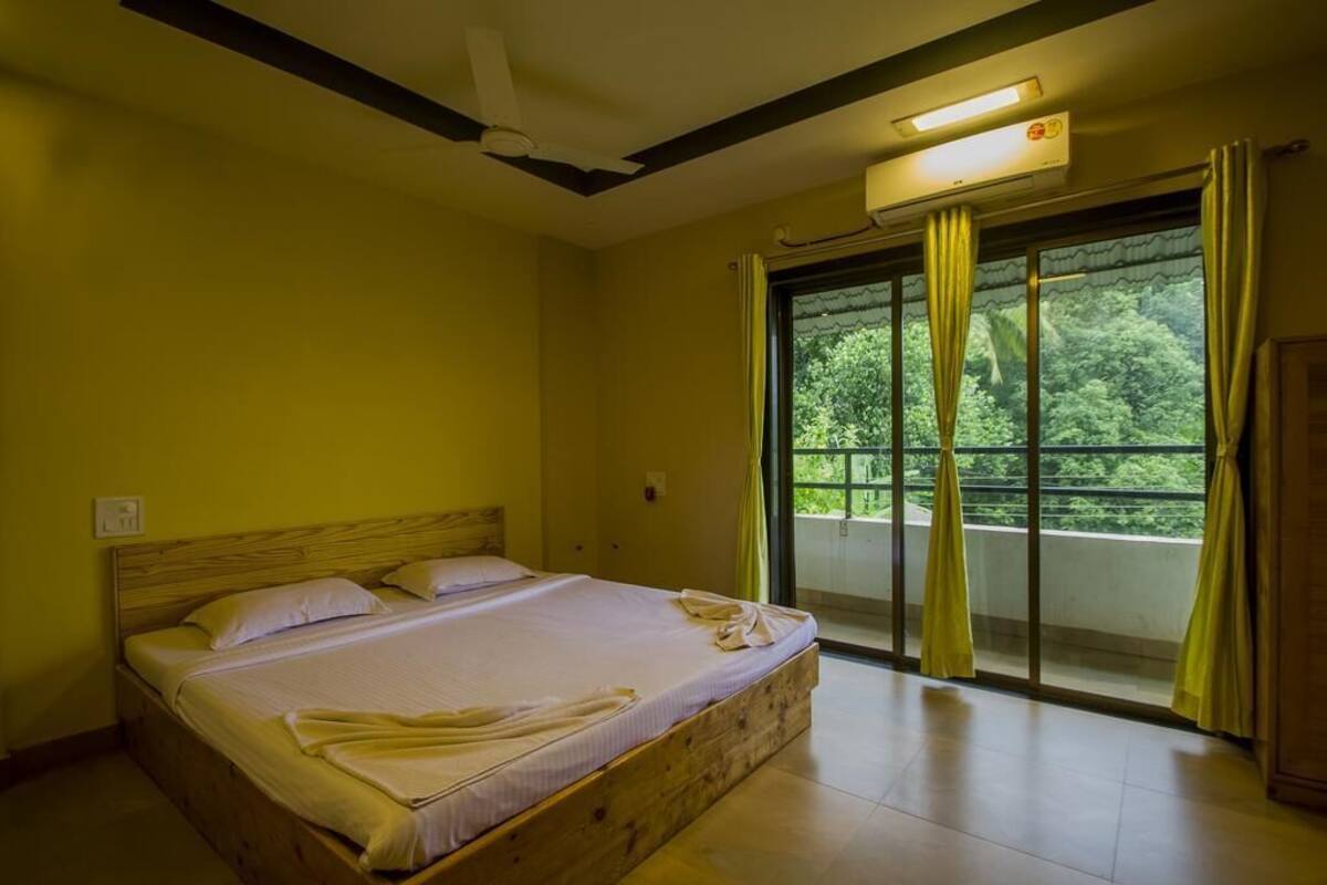 A bedroom with a wooden bed, a ceiling fan, a window with curtains, and a view of greenery outside.