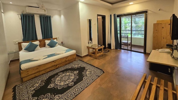 Una camera d'albergo con un letto, una scrivania, una sedia, una ventola a soffitto e vista attraverso una porta in vetro.
