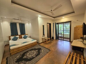 A hotel room with a bed, a desk, a chair, a ceiling fan, and a view through a glass door. - O'NEST Oceano Pearl (Ratnagiri)