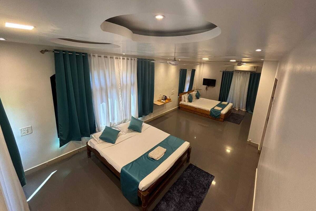 A modern hotel room with a large bed, a smaller bed, a flat-screen TV, and a ceiling light fixture.