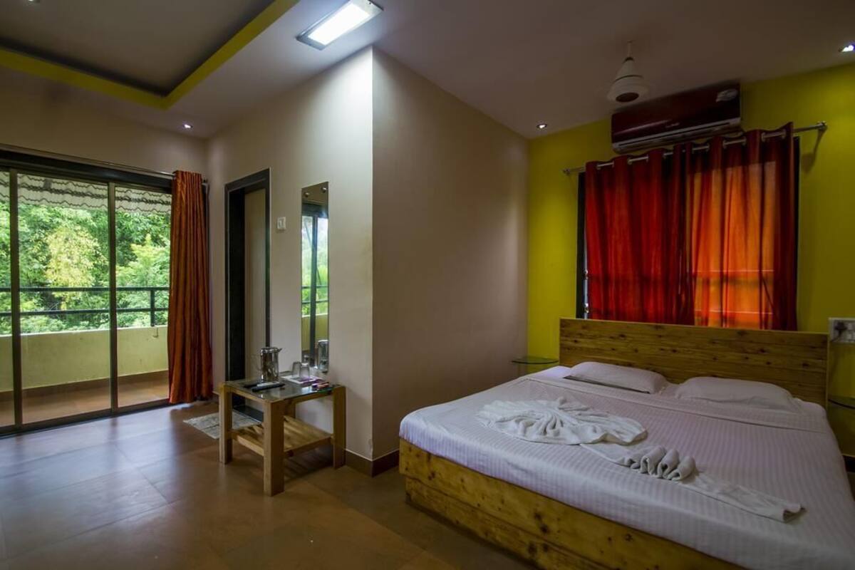 A hotel room with a large window, a wooden bed, a small table, and a mirror.