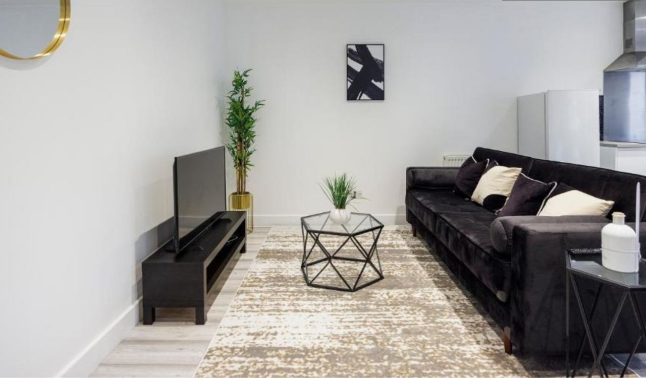 Ett modernt vardagsrum med en svart soffa, ett soffbord i glas och en platt-TV placerad på ett svart TV-bord.
