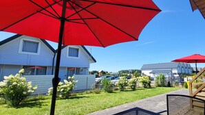 A residential area with a red umbrella, a white house, and a wooden deck.