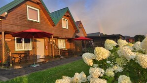 A wooden cabin with a porch, red umbrellas, and white hydrangea bushes.