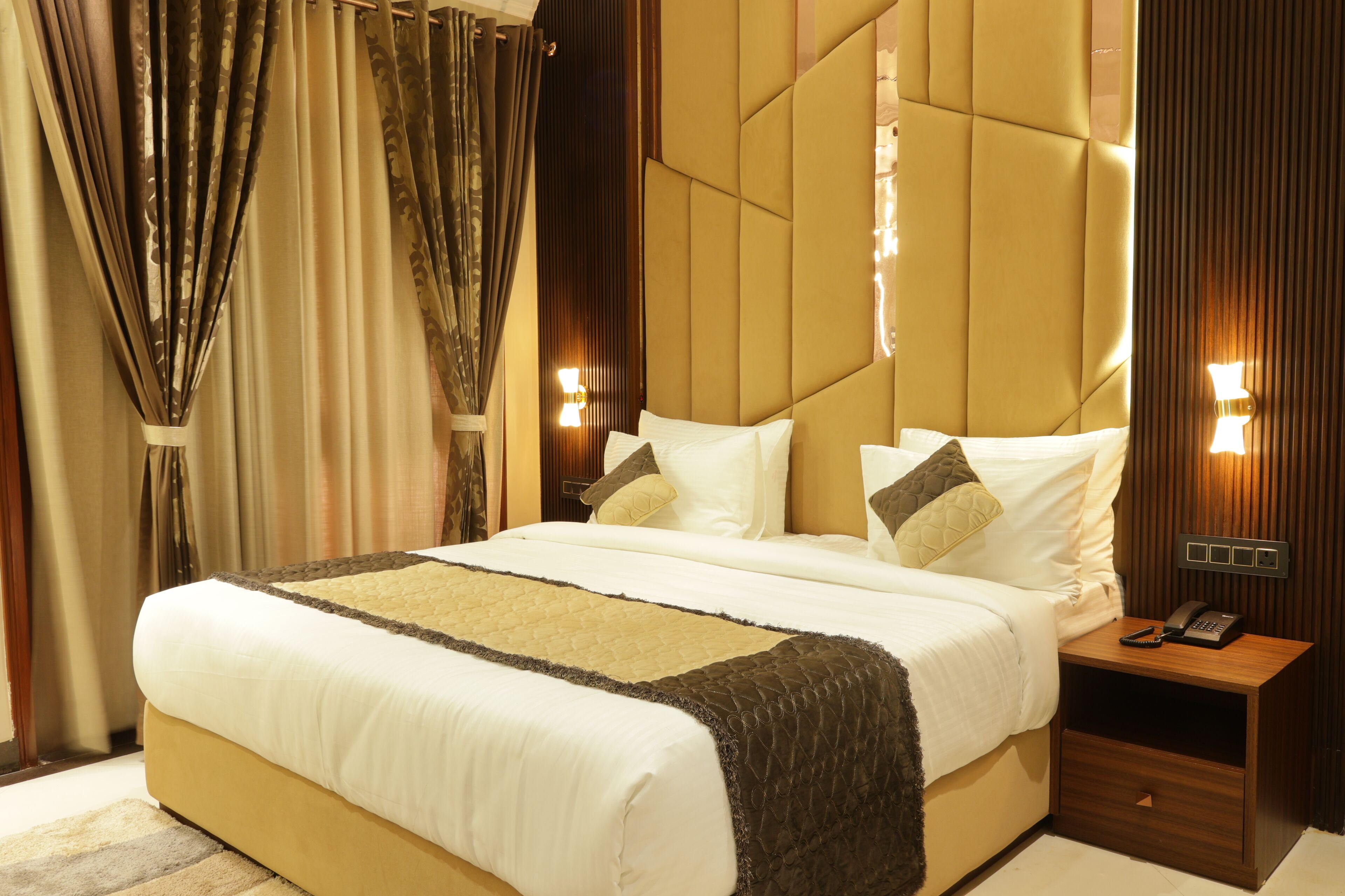 A large bed with a quilted headboard, bedside lamps, and a nightstand with a phone.