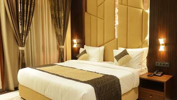 A large bed with a quilted headboard, bedside lamps, and a nightstand with a phone.