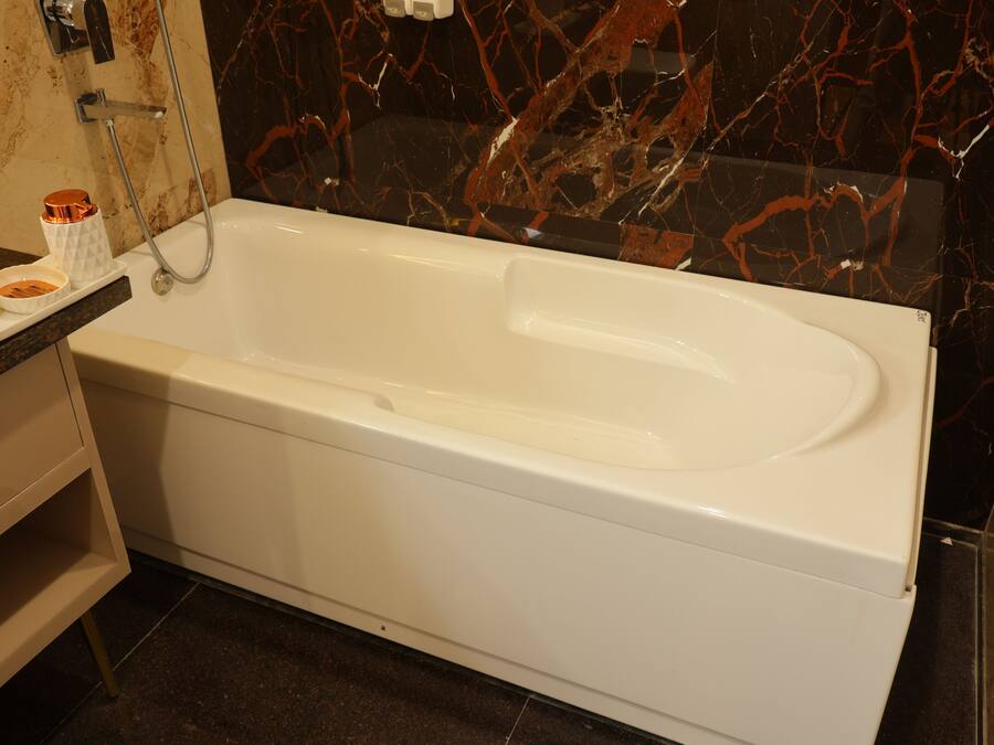 Un baño moderno con una bañera blanca, paredes de mármol y un pequeño estante con artículos de aseo.