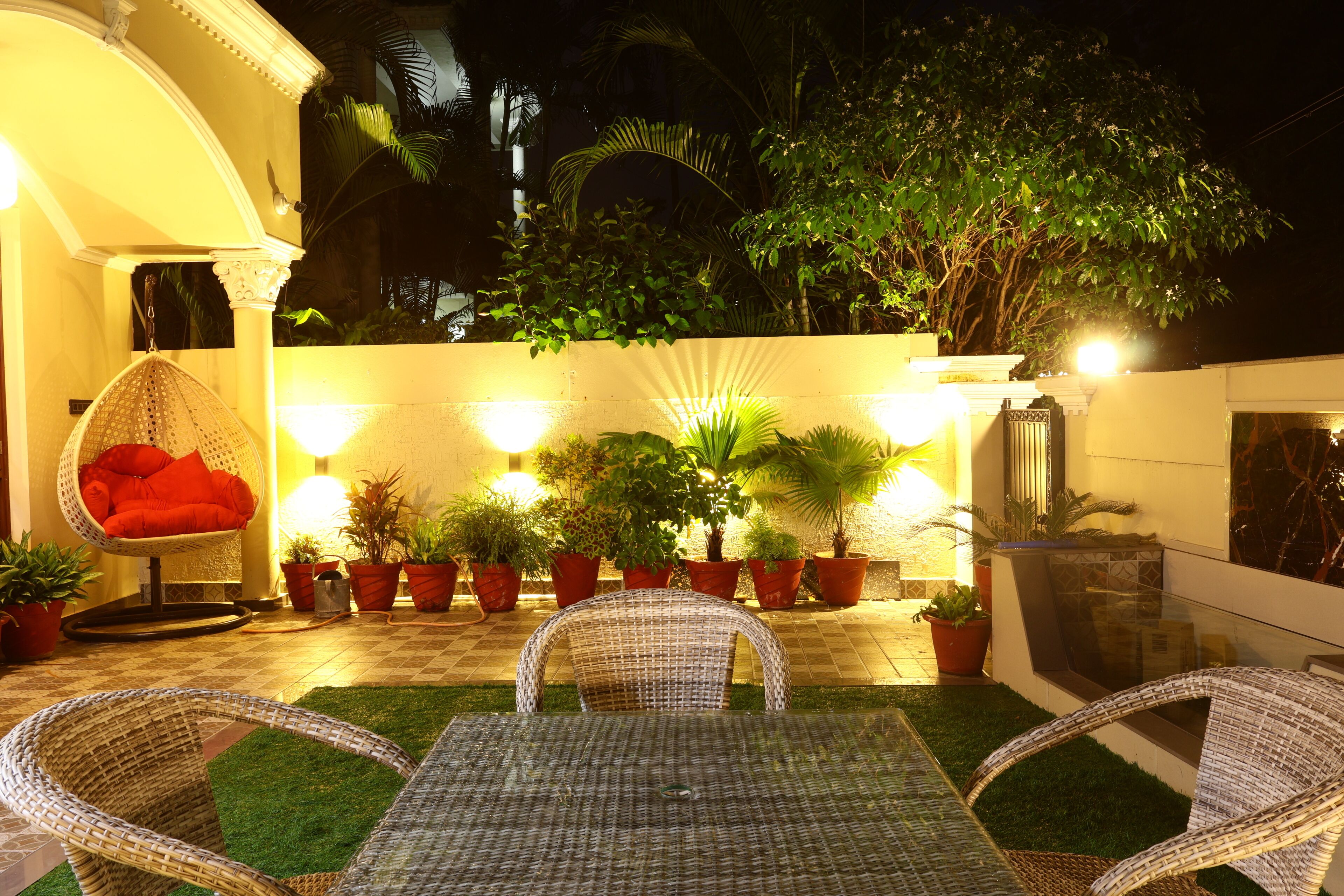 Un patio al aire libre con mobiliario de mimbre, plantas en macetas y piso de baldosas.