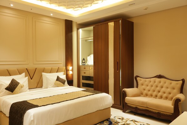 A bedroom with a large bed, a wooden wardrobe, and a leather armchair. - Suramya (Bhopal)