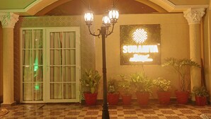 A hotel entrance with a sign reading "SURAMTA," a glass door, and potted plants. - Suramya (Bhopal)