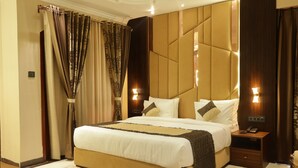 A modern bedroom with a large bed, a nightstand with a phone, and a wall-mounted light. - Suramya (Bhopal)