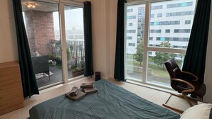 A bedroom with a large bed, a chair, a balcony with a view of buildings, and a ceiling light fixture. - London City Chic Apartment With 3 Bedrooms (London)
