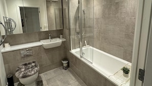 A modern bathroom with a glass-enclosed shower, a bathtub, a toilet with a furry seat, and a sink. - London City Chic Apartment With 3 Bedrooms (London)