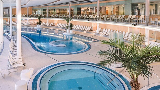 A pool area with multiple swimming pools, lounge chairs, and palm trees.
