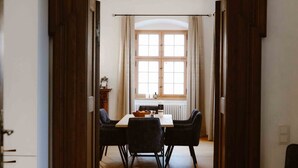 A dining area with a wooden table and chairs, a window with curtains, and a radiator.