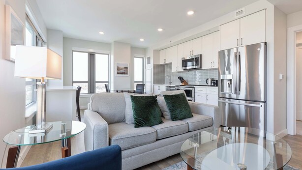 A modern kitchen with stainless steel appliances, a glass dining table, and a grey sofa with green cushions. - Private Apt Downtown (Quincy)