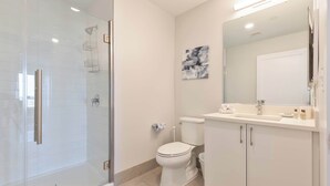 A modern bathroom with a glass shower enclosure, a toilet, and a vanity with a mirror. - Private Apt Downtown (Quincy)