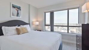A hotel room with a large bed, a nightstand with a lamp, a dresser, and a large window offering a city view. - Private Apt Downtown (Quincy)