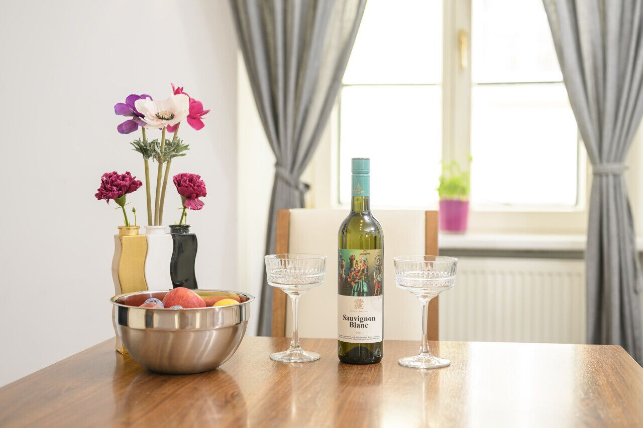 Une table avec une bouteille de vin, deux verres, un saladier de fruits et trois vases de fleurs.