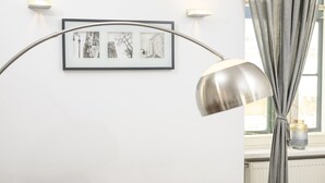 Una habitación con una obra de arte en blanco y negro de un paisaje urbano enmarcada en la pared, una lámpara de pie moderna y una ventana con cortinas.