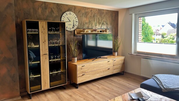 Una sala de estar con un aparador de madera, un televisor y una ventana con vistas a casas.