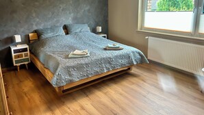 Un dormitorio con cama, mesitas de noche de madera, una ventana con vistas y un radiador.
