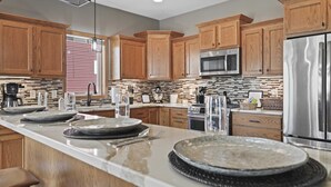 A modern kitchen with wooden cabinets, stainless steel appliances, and a large island with dining setup. - 25min to Capitol - KING Suite - Game Room - Groups (Stoughton)