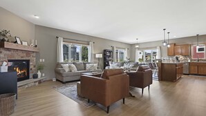 A spacious living room with a fireplace, a sofa, and a coffee table. There is a kitchen area with wooden cabinets and a dining area with a table and chairs. - 25min to Capitol - KING Suite - Game Room - Groups (Stoughton)