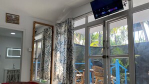 Een hotelkamer met een bed, een televisie, een groot raam met gordijnen, een spiegel en uitzicht op buiten.
