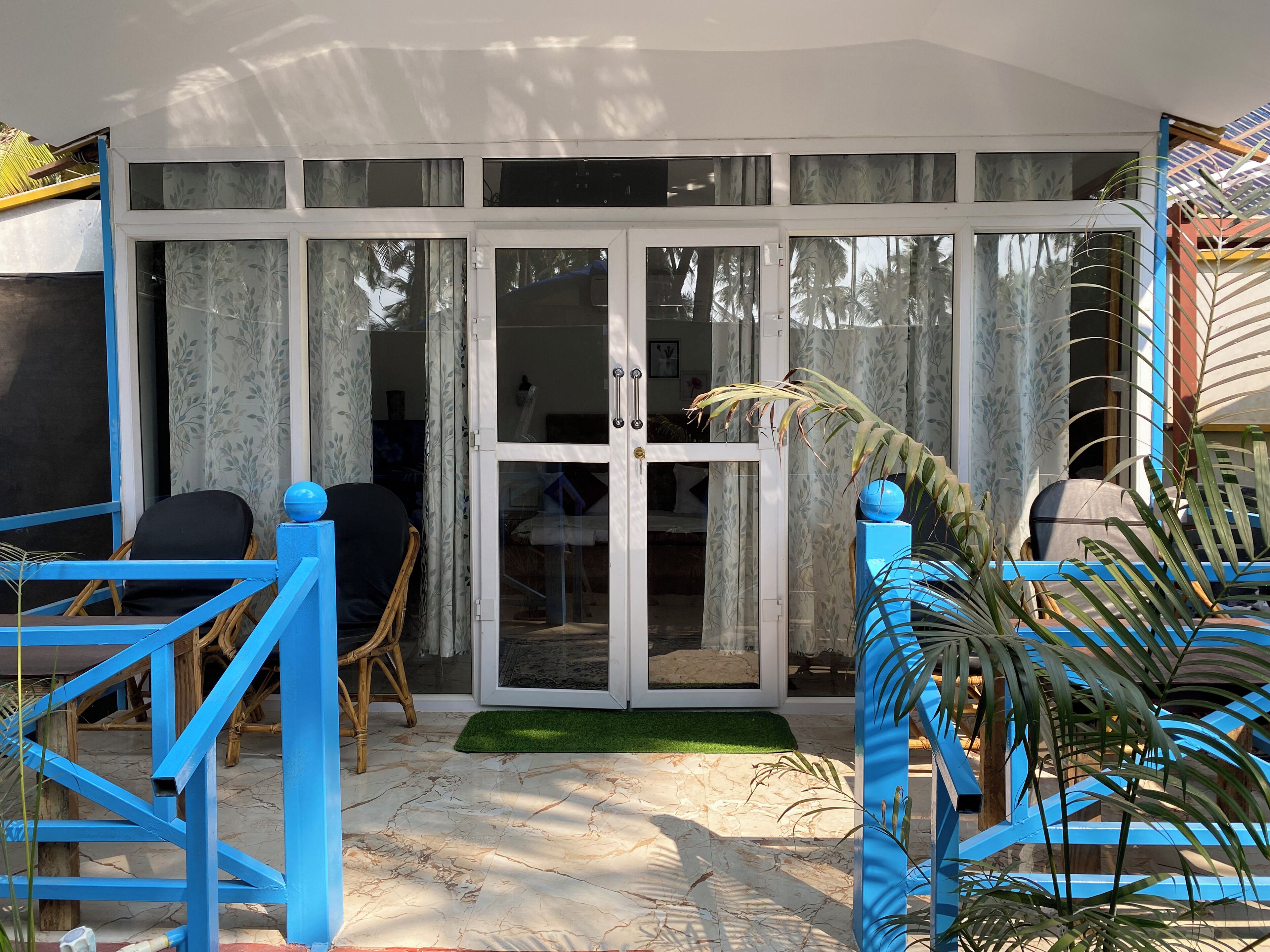 Una habitación con puerta de vidrio corredera, una silla azul, una mesita y un tapete verde.