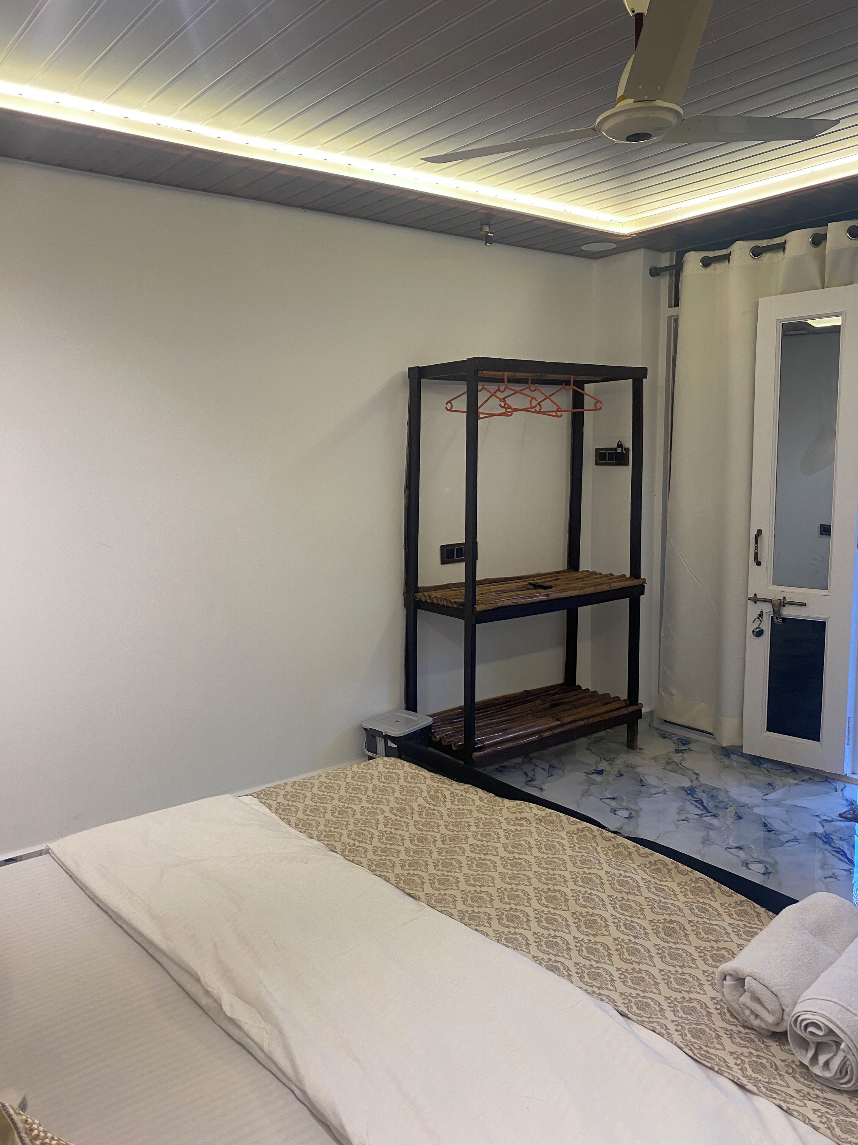 A room with a bunk bed, a small table, a ceiling fan, and a door with curtains.