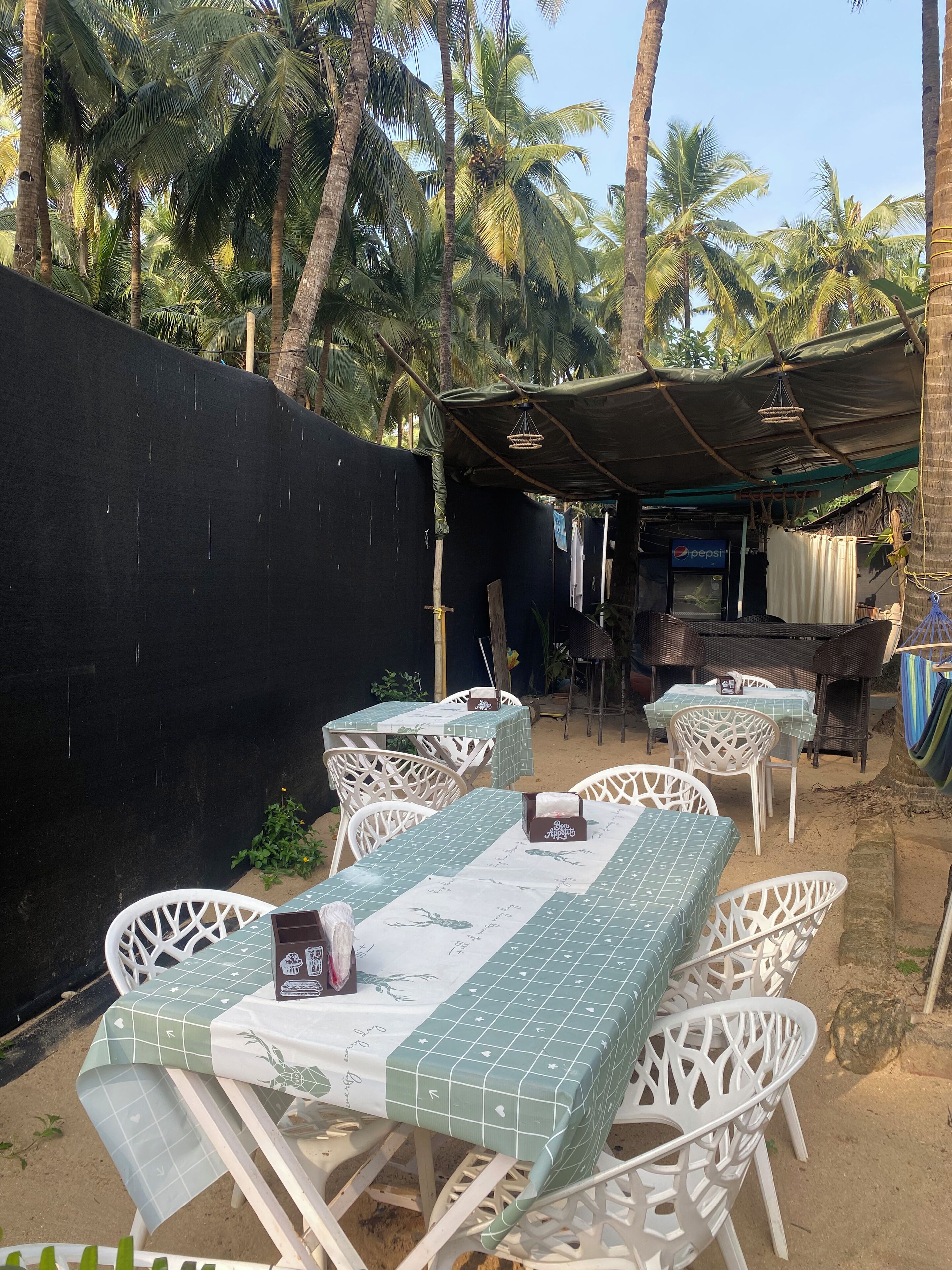 Un espace extérieur aménagé avec des chaises et des tables en plastique blanc, recouvertes de nappes à carreaux verts et blancs.