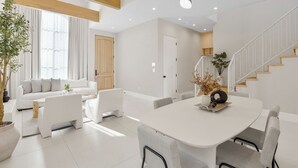 A modern living room with a white sofa, grey armchairs, a dining table, and a staircase. - Villa Camellia - Charming 5 BR Home in the Heart of Studio City (Studio City)