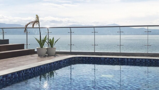 A swimming pool with a tiled edge, potted plants, and a view of the sea.