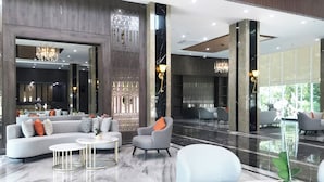 A modern lobby with a marble floor, grey sofas, armchairs, and a chandelier.