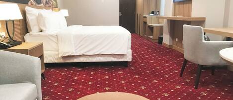 Une chambre d’hôtel avec un lit, un bureau, une chaise et un téléviseur fixé au mur.