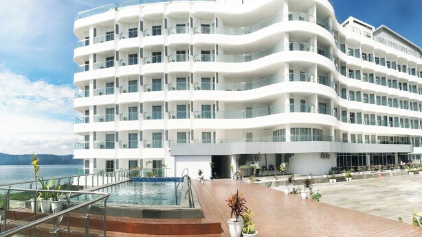 A multi-story hotel with balconies, a pool, and a view of the sea.
