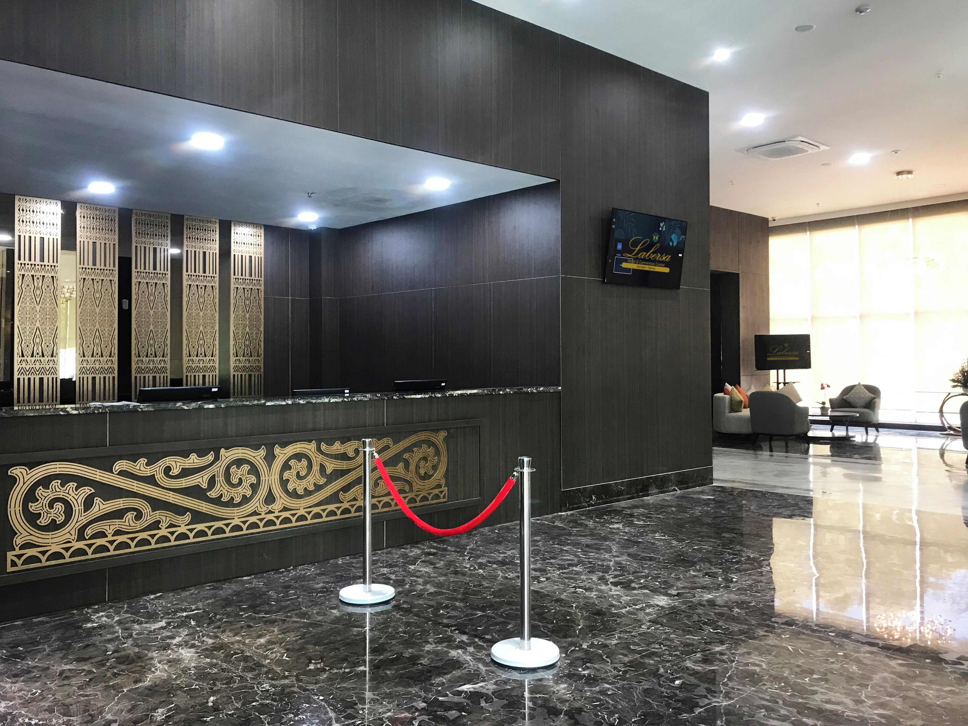 Zona de recepción con un panel de madera oscura, suelo de mármol y una barrera de cuerda roja.