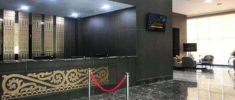 A reception area with a dark wood panel wall, a marble floor, and a red rope barrier.