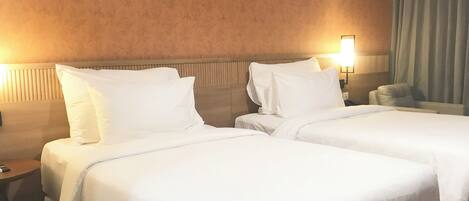 A hotel room with two beds, a nightstand, a lamp, and a view of the outdoors.