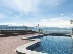 A pool with a tiled edge, surrounded by a wooden deck and potted plants.